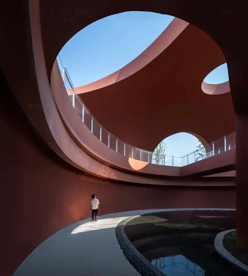 Visitor standing in circular courtyard beneath sweeping red concrete balconies and multiple oval roof apertures