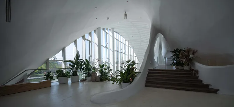 Interior lobby with potted plants along floor-to-ceiling windows and timber staircase under vaulted ceiling