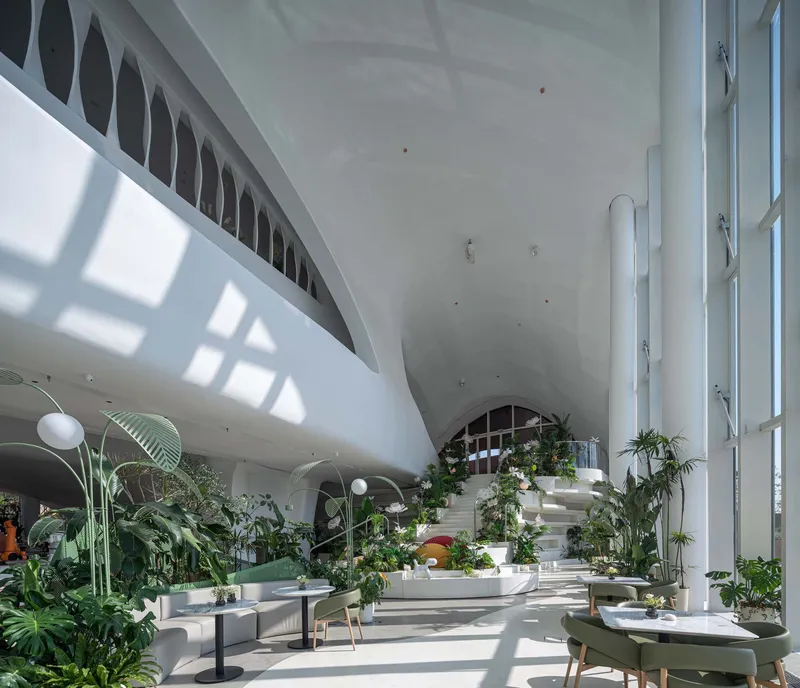Double-height interior with vaulted ceiling, white columns, and potted plants scattered across the floor