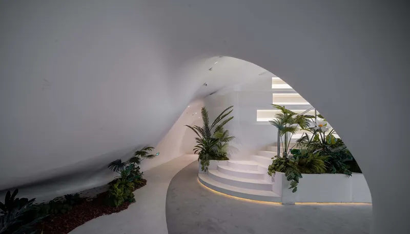 Curved white staircase framed by an arched opening with planted beds along the edges