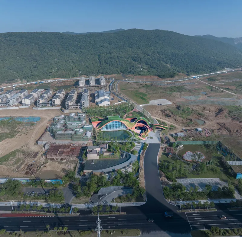 Aerial view of the ribboning roof structure set among wooded hillsides and developing landscape