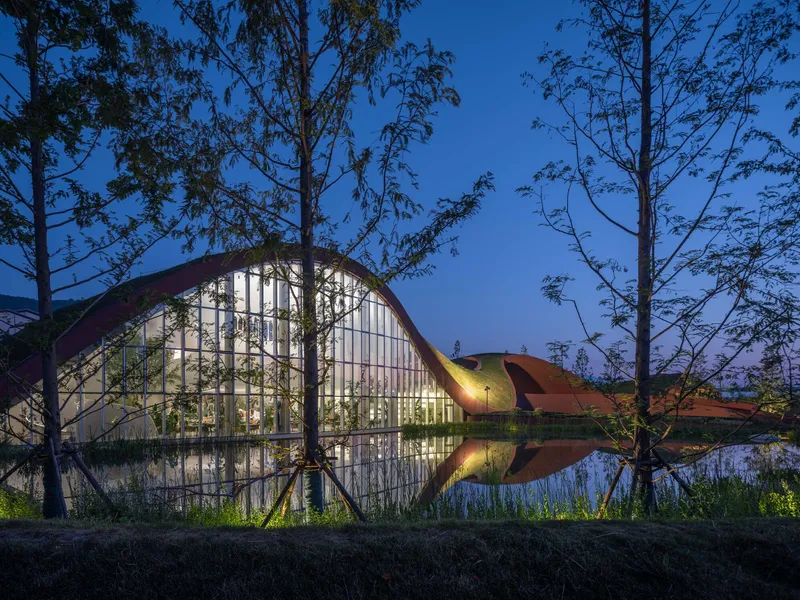 Glazed facade reflecting in the pond with surrounding trees silhouetted against the twilight sky