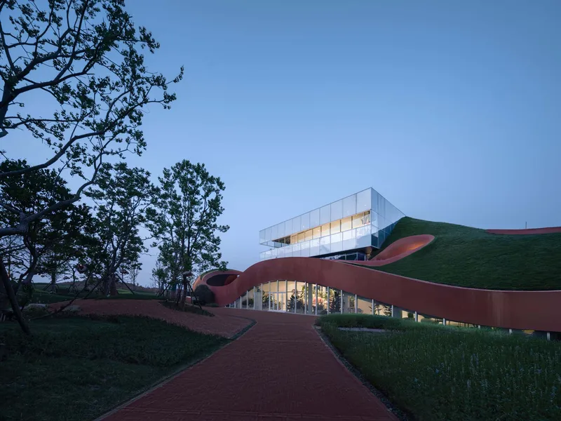 Approach path winding through the undulating roof forms toward the glass pavilion at twilight