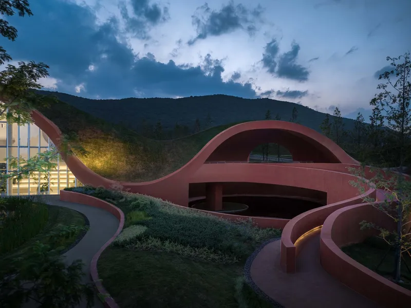 Planted roof with undulating terracotta surfaces and curved pathways at dusk beneath a mountain ridge