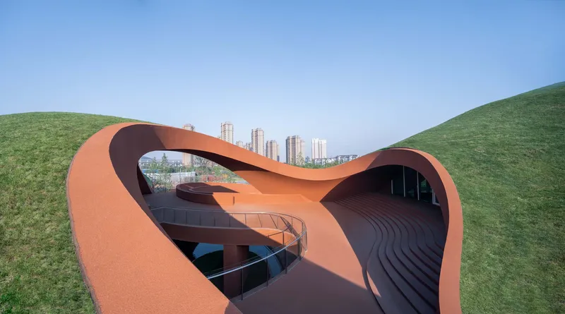 Ribbon staircase and terracotta canopy framing the amphitheater between two grass-covered mounds