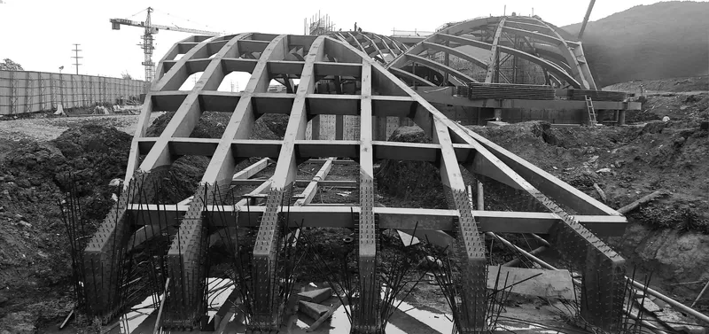 Exposed steel frame structure under construction on excavated ground with mountains behind
