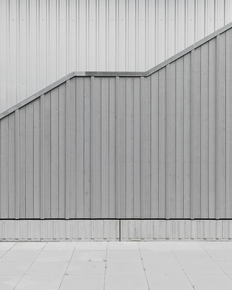 Exterior detail of vertical metal panel facade with angular roofline meeting concrete pavers