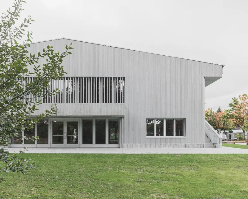 Facade with vertical batten screen balcony above glazed ground floor openings framed by trees