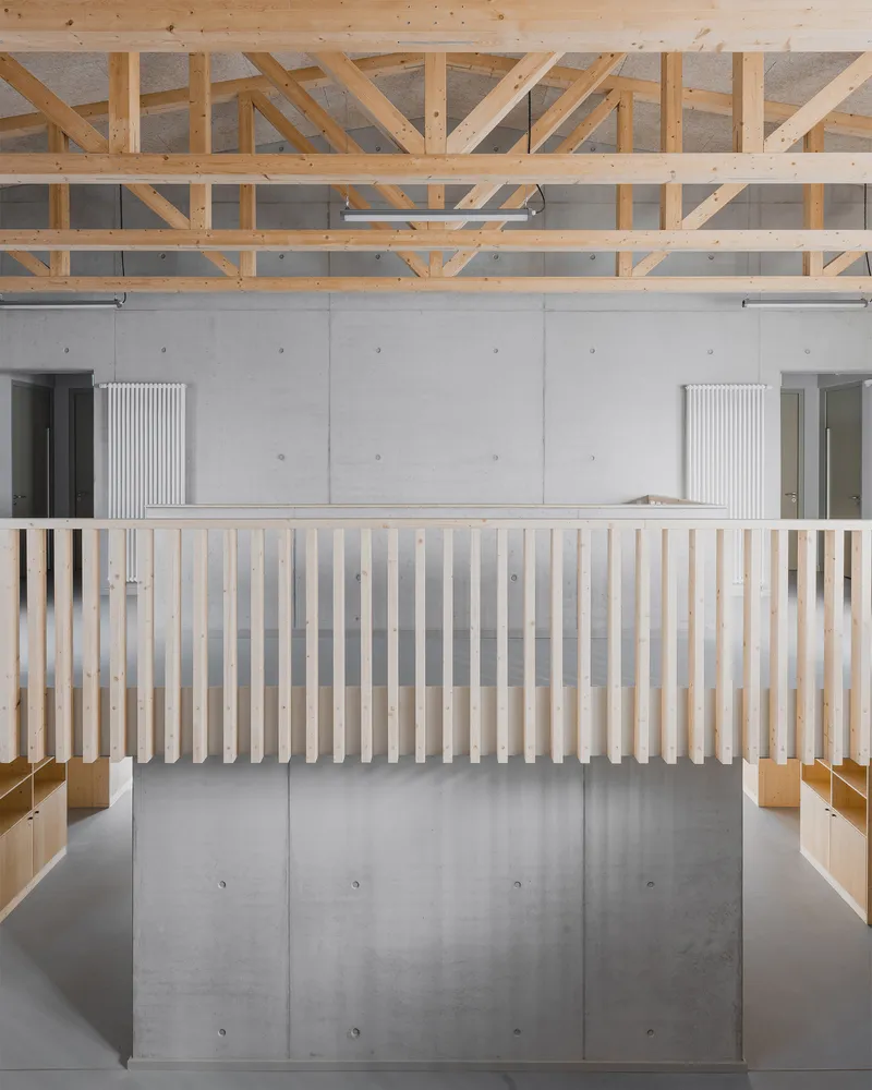 Double-height interior with timber truss ceiling, concrete wall panels, and vertical slat balustrade