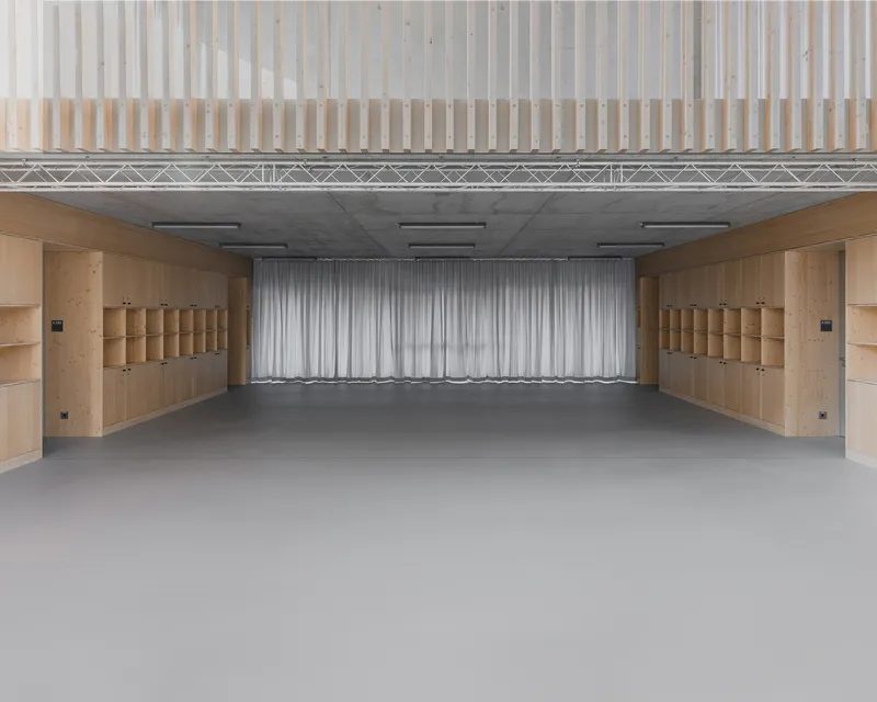 Empty hall with plywood shelving units along both walls and gray curtain at the end
