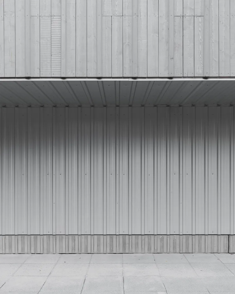 Covered entry with vertical metal cladding and weathered timber facade above a concrete paver courtyard