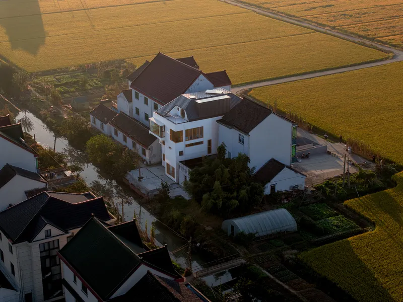 Aerial view at sunset showing the clustered white volumes and pitched roofs surrounded by farmland and waterways