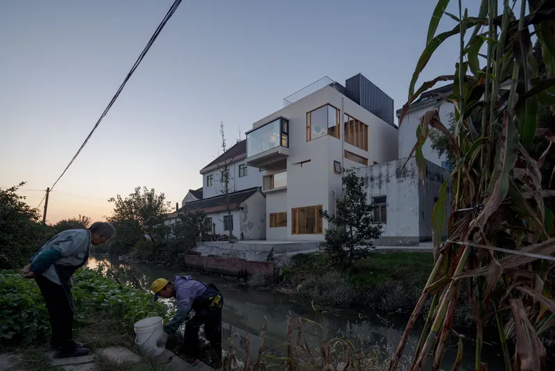 Rear elevation at dusk with residents gathering by the canal edge below the illuminated timber window frames