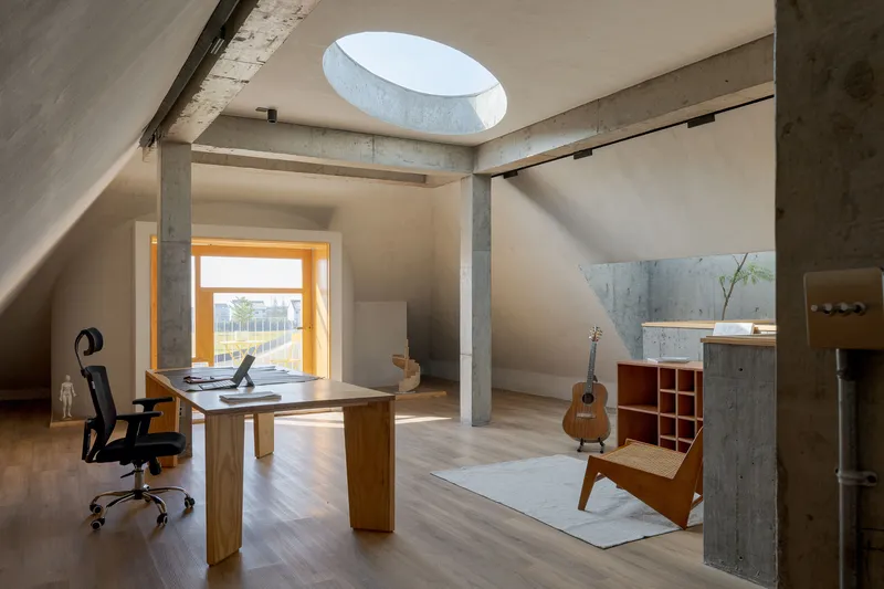 Home office with timber desk and acoustic guitar beneath circular skylight and exposed concrete columns