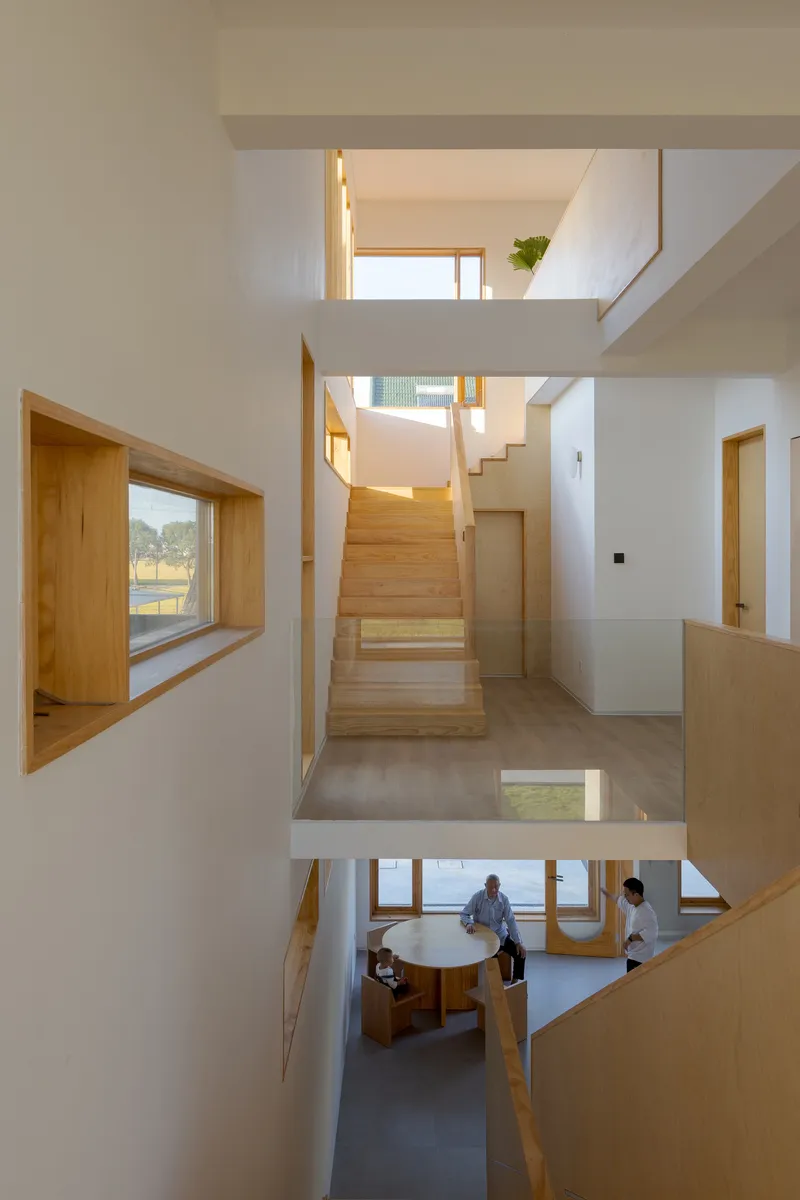 Triple-height void showing timber staircase connecting multiple levels with framed window openings