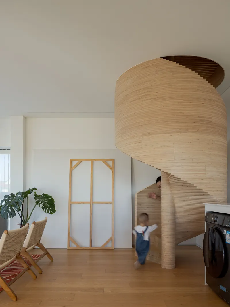 Cylindrical sculptural staircase wrapped in laminated timber slats with child running past