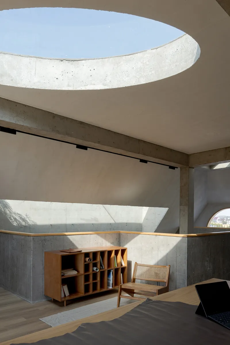 Curved concrete ceiling oculus opening to sky above horizontal window and timber storage credenza