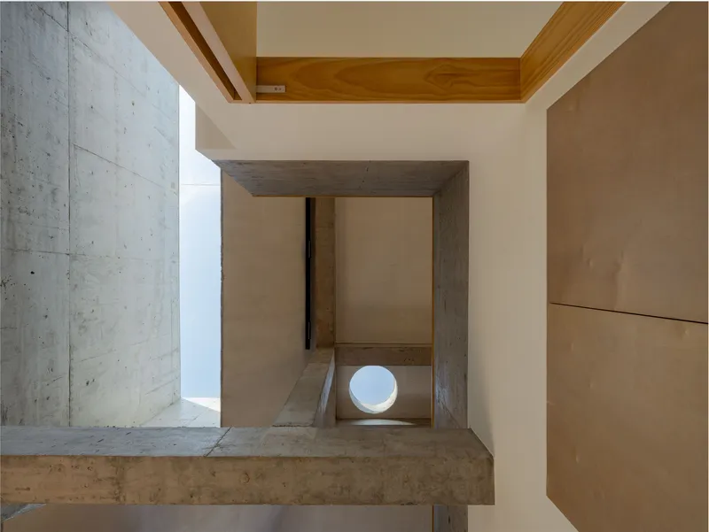 View down through a concrete frame opening showing timber stairs and a circular window below
