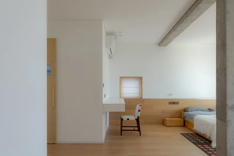Bedroom with built-in timber platform bed and exposed concrete ceiling beam beside white walls