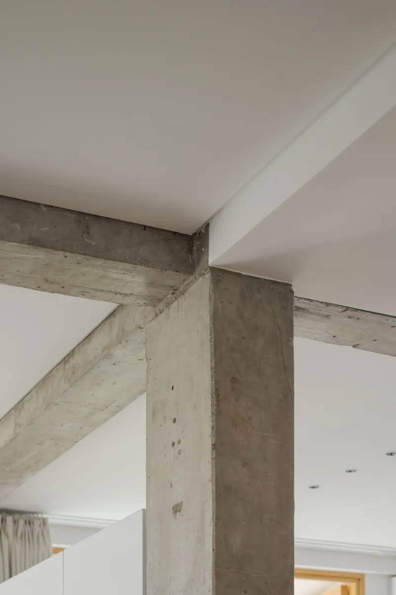 Close-up of exposed concrete beams and column intersecting white ceiling planes at multiple angles