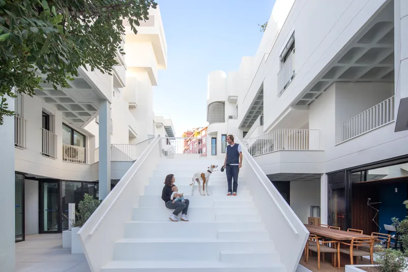 Wide white staircase between housing blocks with residents and a dog under clear blue sky