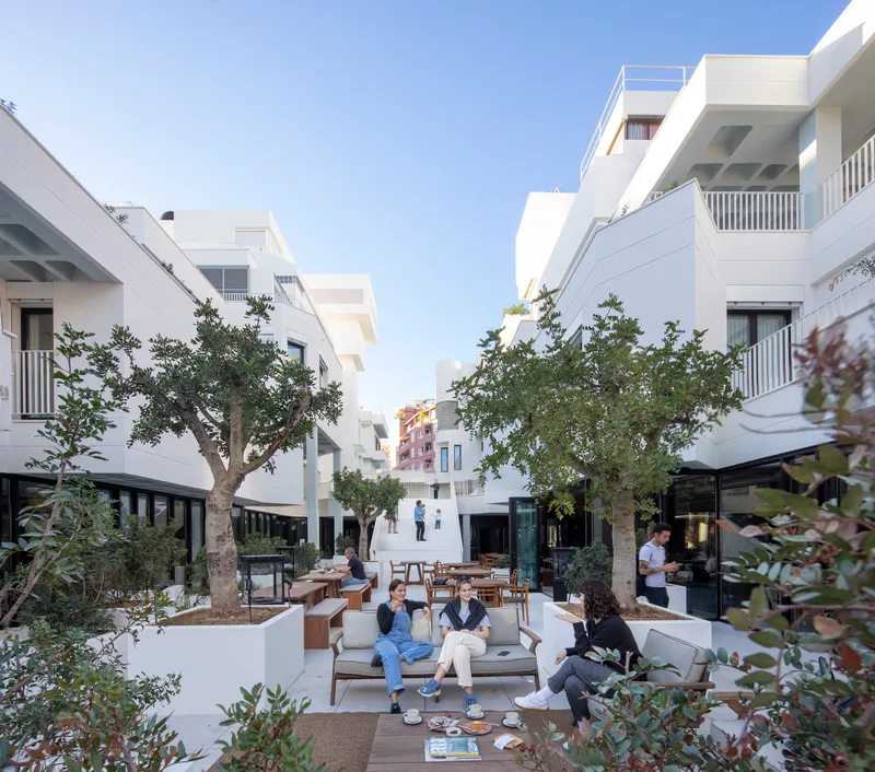 Courtyard with planted trees and residents seated on benches between white residential wings