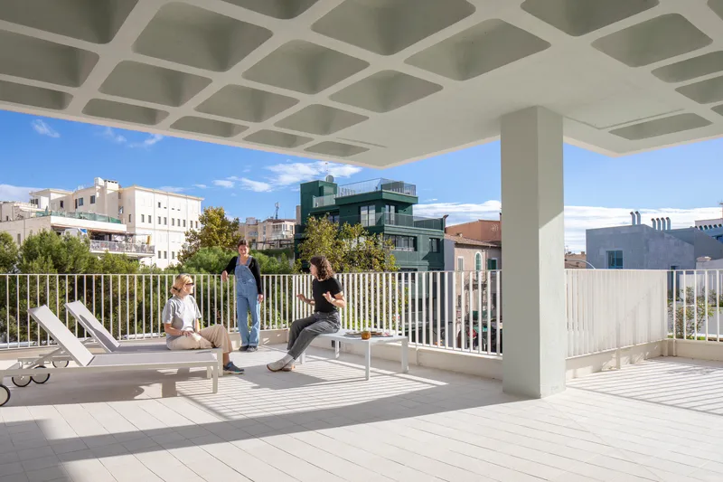 Rooftop terrace with coffered concrete ceiling and white vertical railing under midday sun