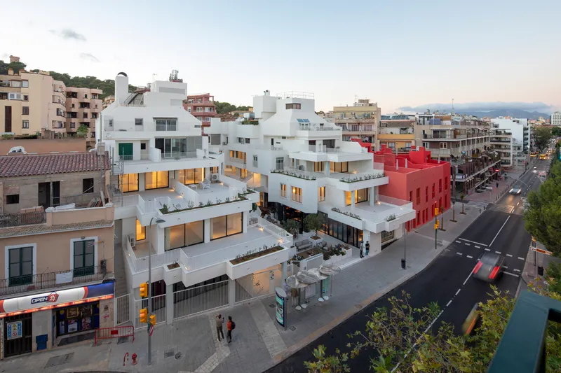 Elevated view of white terraced housing volumes with illuminated interiors at dusk between older neighborhood buildings