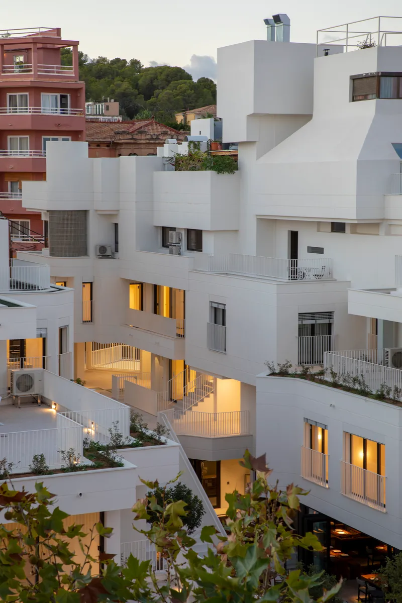 Stacked white volumes with planted terraces and warm interior lighting at twilight