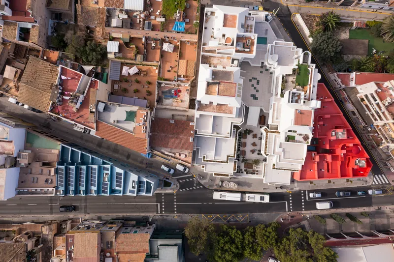 Aerial view of clustered white rooftops meeting a red building and street intersection below