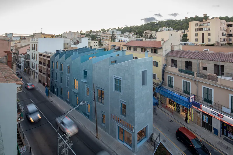 Gridded tile facade on a corner building with moving traffic and pedestrians at dusk