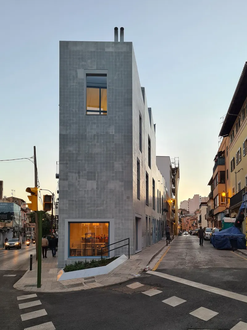 Street corner view of a narrow tiled tower with ground floor glazing at dusk