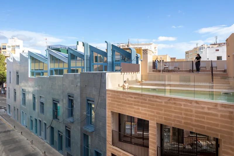 Rooftop terrace with glass railings and swimming pool overlooking sawtooth glazed volumes under afternoon light