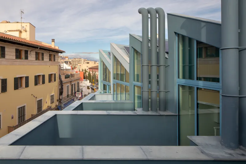 Rooftop terrace showing three industrial ducts and angled glass pavilions against a cloudy sky