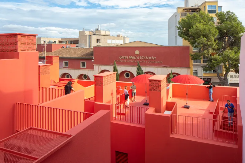 Rooftop platforms in red and orange with corrugated metal screens and visitors under cloudy sky