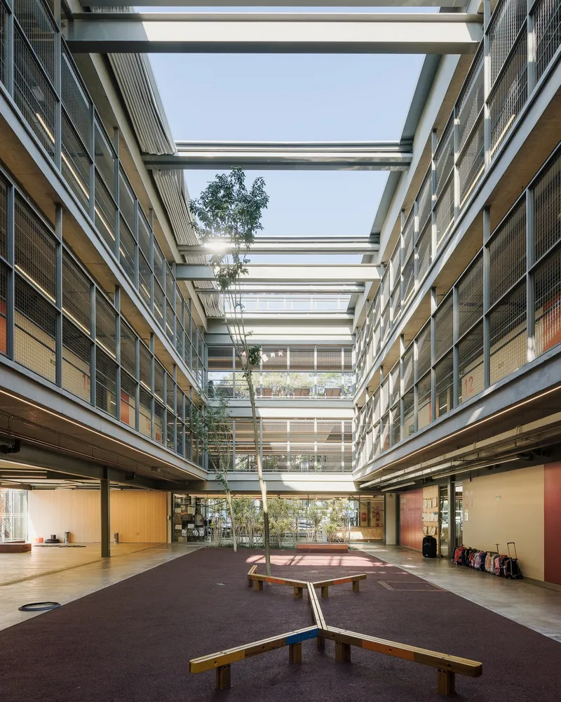 Central courtyard with timber benches and planted trees beneath horizontal roof beams spanning four levels