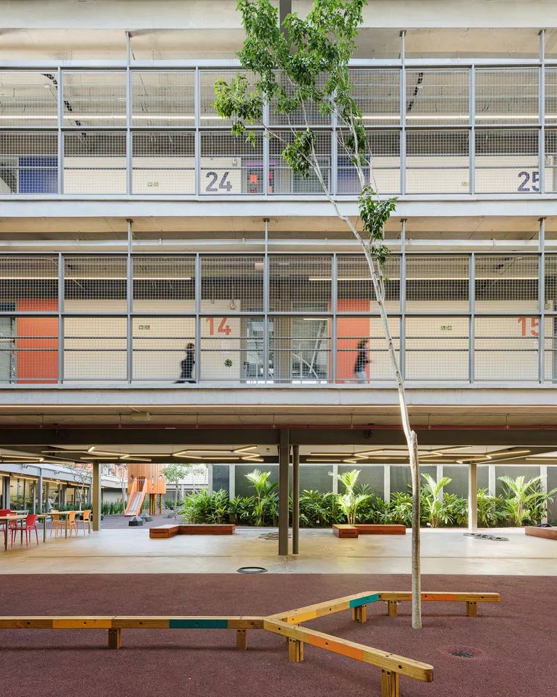 View across the courtyard showing numbered classrooms with mesh screens and orange accent doors facing the open space