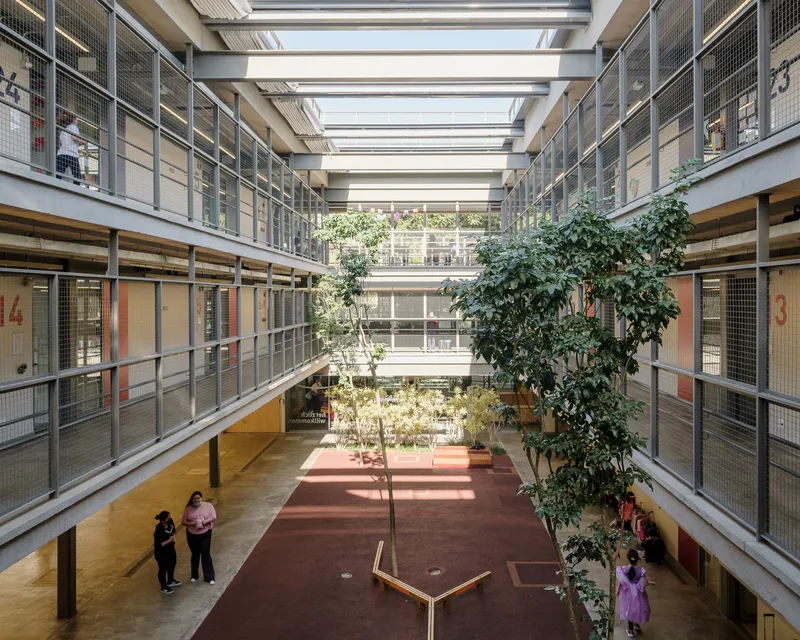 Interior courtyard atrium with circulation balconies, wire mesh railings, and planted trees under skylight beams