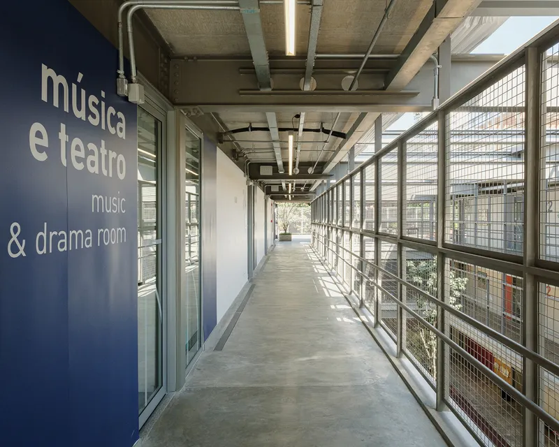 Concrete corridor with exposed ceiling ducts and mesh railing overlooking the courtyard below
