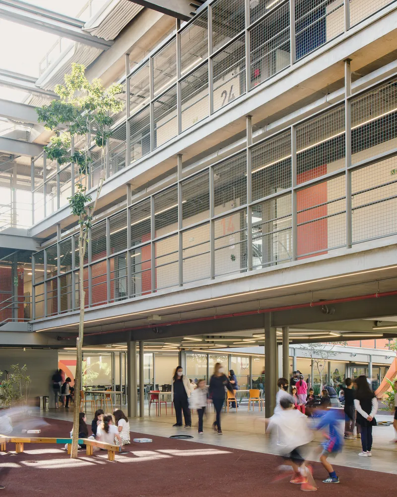 Ground floor courtyard with motion-blurred children and adults gathered beneath stacked classroom balconies
