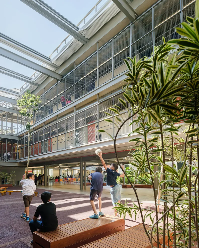 Courtyard with mesh-screened balconies and students playing basketball beneath planted trees and a glazed canopy