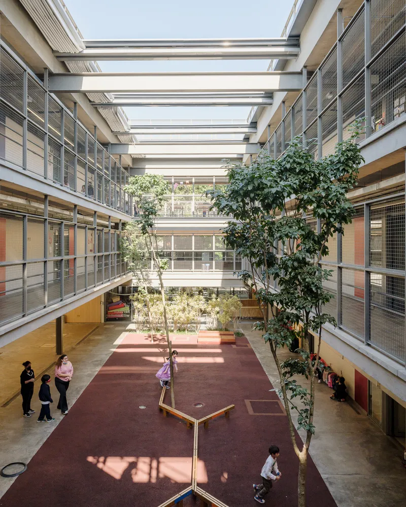 Long view down the internal courtyard with planted trees casting shadows on the maroon floor surface