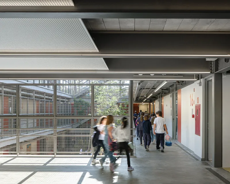 Internal corridor with mesh screen to courtyard and students walking in motion blur beneath exposed structural beams
