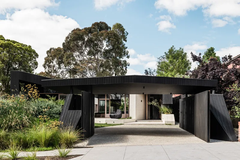 Entry driveway framed by angular black timber columns supporting the flat cantilevered roof plane above