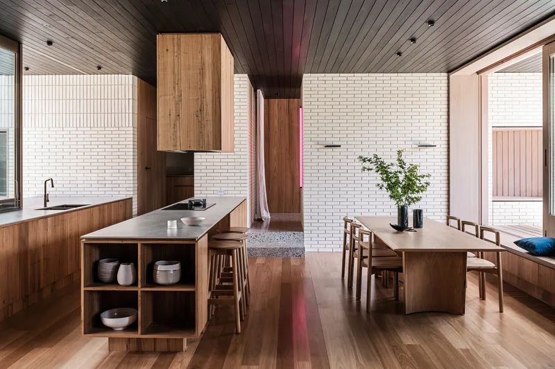 Open kitchen and dining area with timber cabinetry, white brick walls and a dark timber slatted ceiling