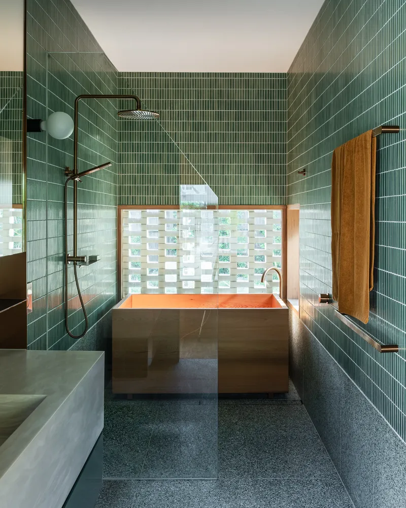 Bathroom with green vertical tile walls, copper bathtub and a translucent glass block window behind