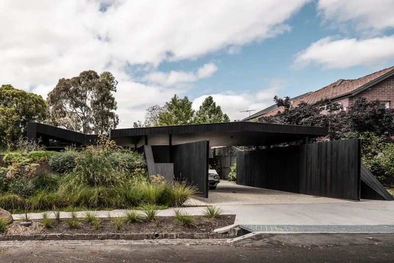 Street view of the cantilevered carport with vertical timber cladding and native grasses along the driveway
