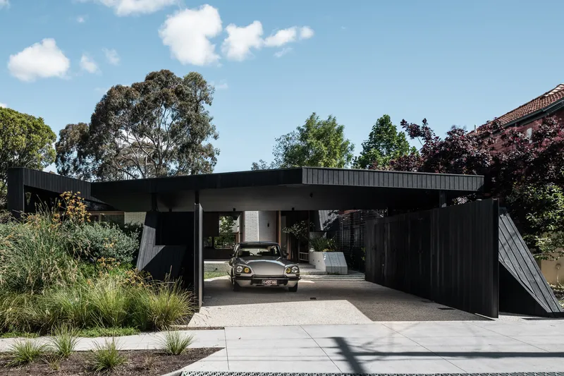 Open carport sheltering a car beneath the projecting roof plane with planted beds on either side