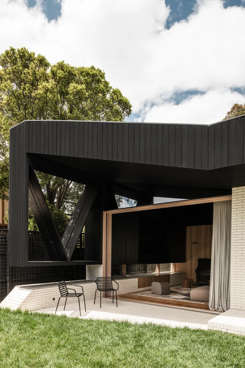 Rear terrace showing diagonal structural bracing beneath the timber overhang and sliding glass doors to the living room