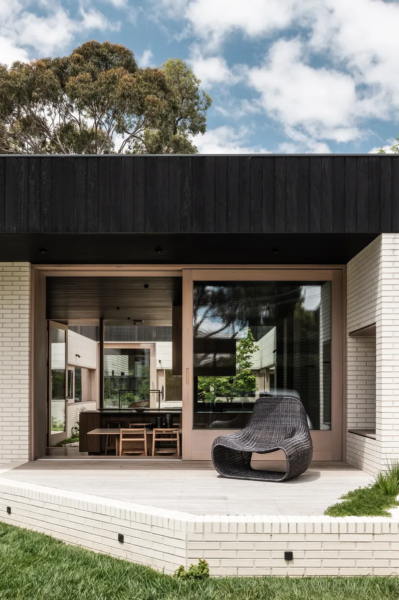 Covered patio with timber-framed openings revealing the dining area beyond and a woven lounge chair on deck